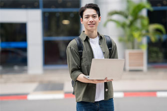 Male student outside holding laptop happy