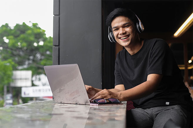 Male outside sitting on laptop headphones